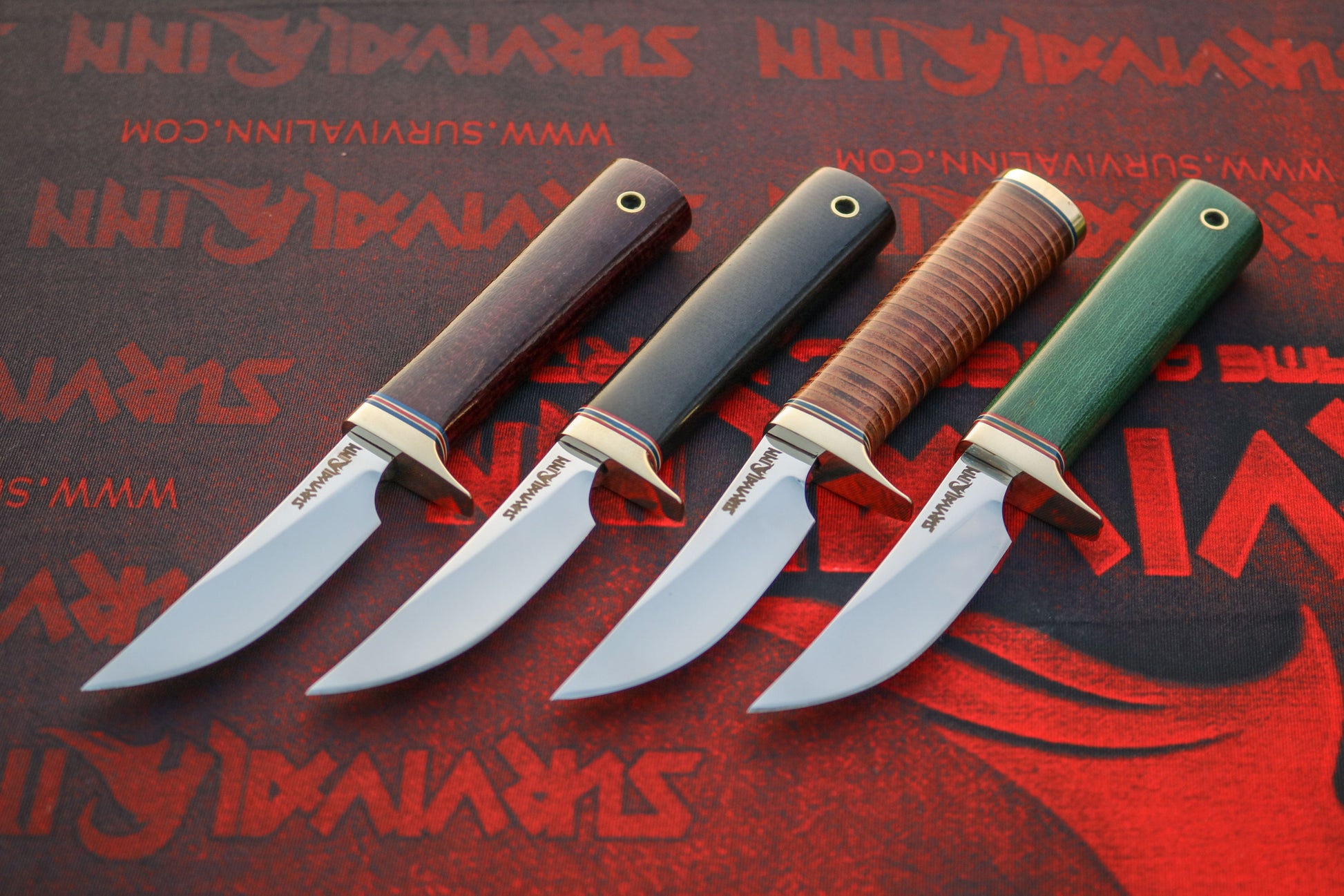 Four Randall Model 20 Yukon Skinner style knives with brown micarta, black micarta, stacked leather, and green micarta handles displayed together